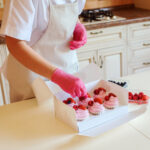The process of cooking delicious cupcakes with whipped fruit cream, decorated with raspberries,strawberries and blueberries. Homemade appetizing dessert packed in white box. Desserts delivery.