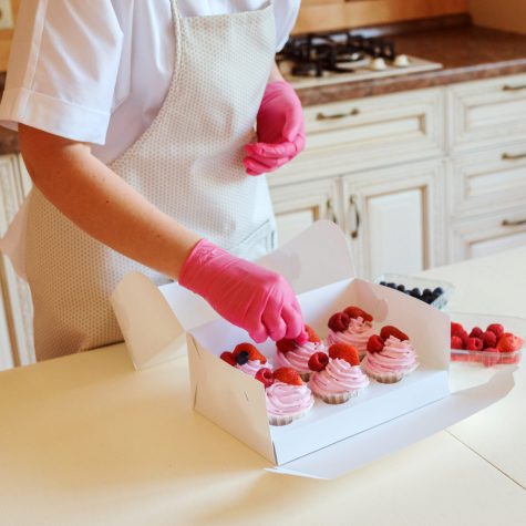 The process of cooking delicious cupcakes with whipped fruit cream, decorated with raspberries,strawberries and blueberries. Homemade appetizing dessert packed in white box. Desserts delivery.